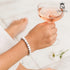 Feines Howlith-Armband mit weißen Perlen am Handgelenk mit Rosé-Weinglas – sommerlich, stilvoll, entspannt uniqal